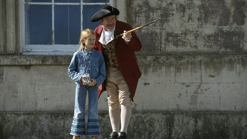 A small girl with a man in c18th costume, he is pointing out something to her with a cane, in front of the house at Castle Ward